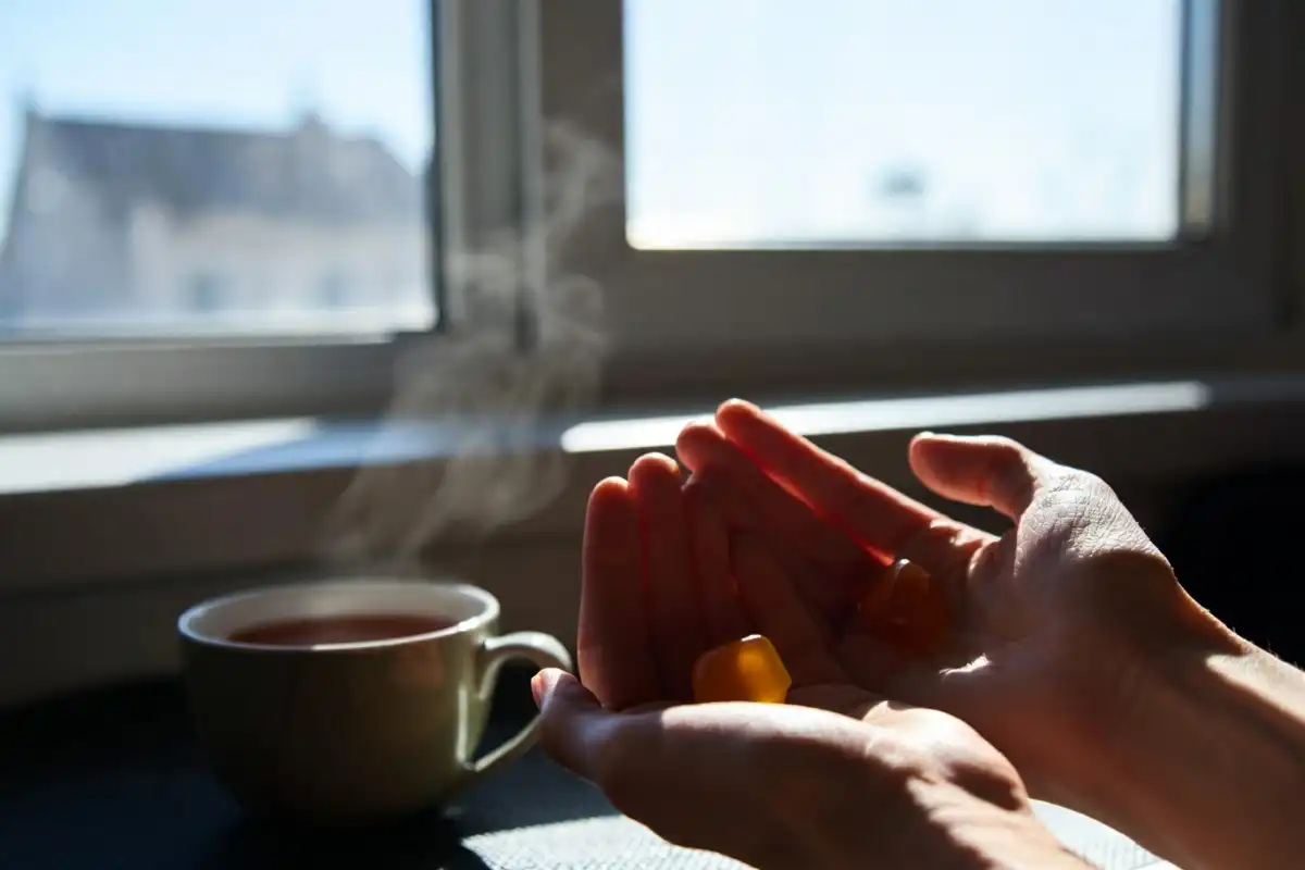 Person holding ashwagandha Nature Made gummies with a warm tea cup at sunrise