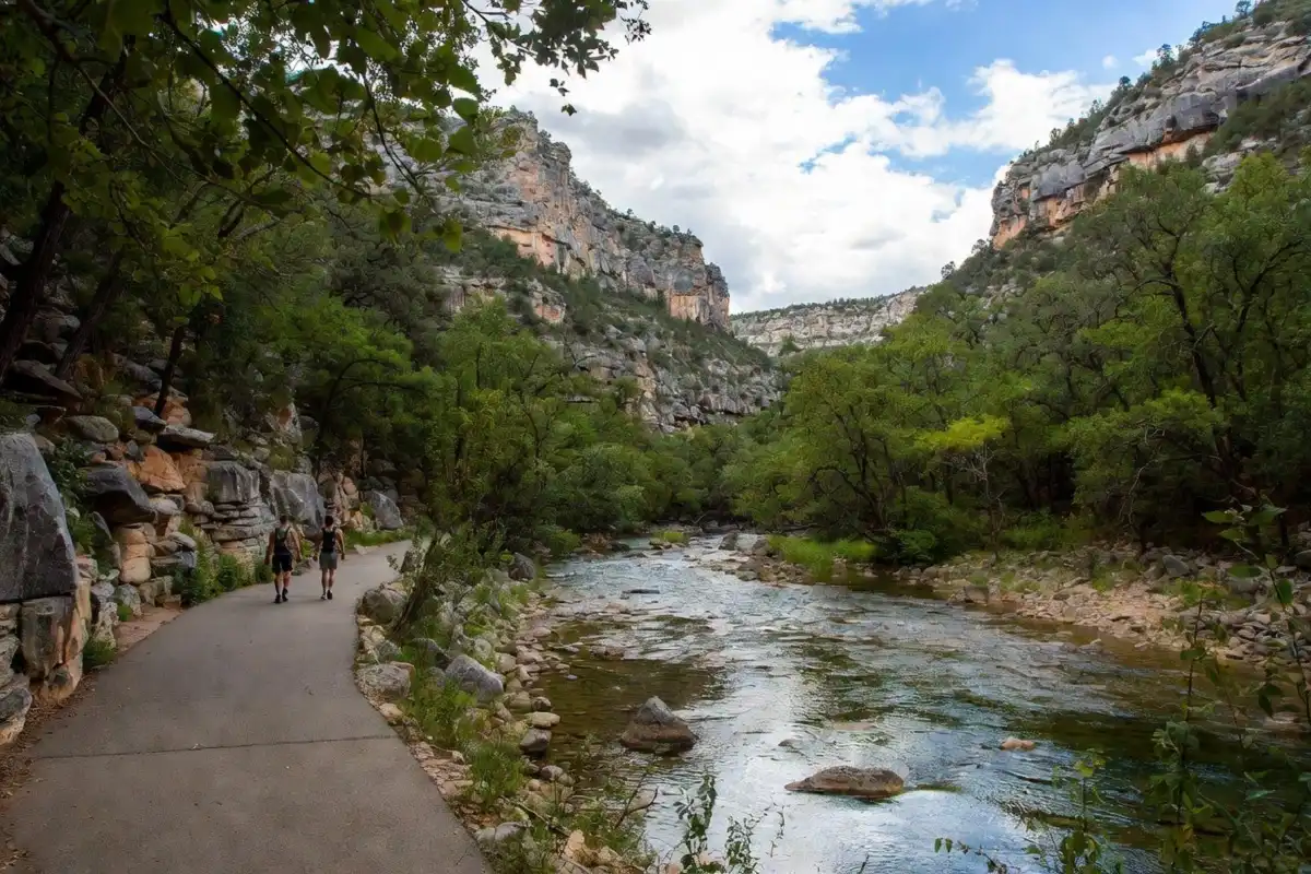 Hikers on a paved trail alongside a clear stream with limestone bluffs in the background