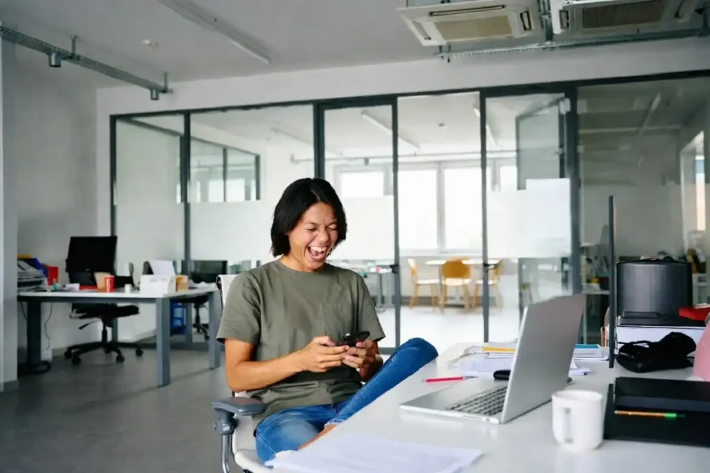 Person laughing while sharing happy friday gifs on their phone at work