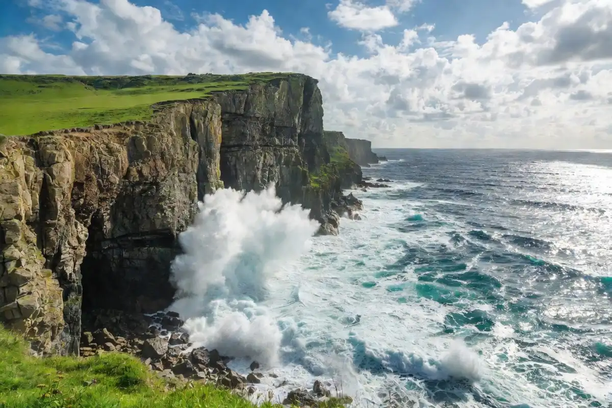 Dramatic coastal cliffs with crashing waves and a bright blue sky in the background