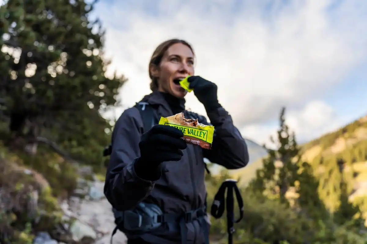 Person eating a Nature Valley protein bar while hiking on a scenic nature trail