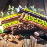 Assorted Nature Valley protein bars arranged on a wooden table with natural sunlight