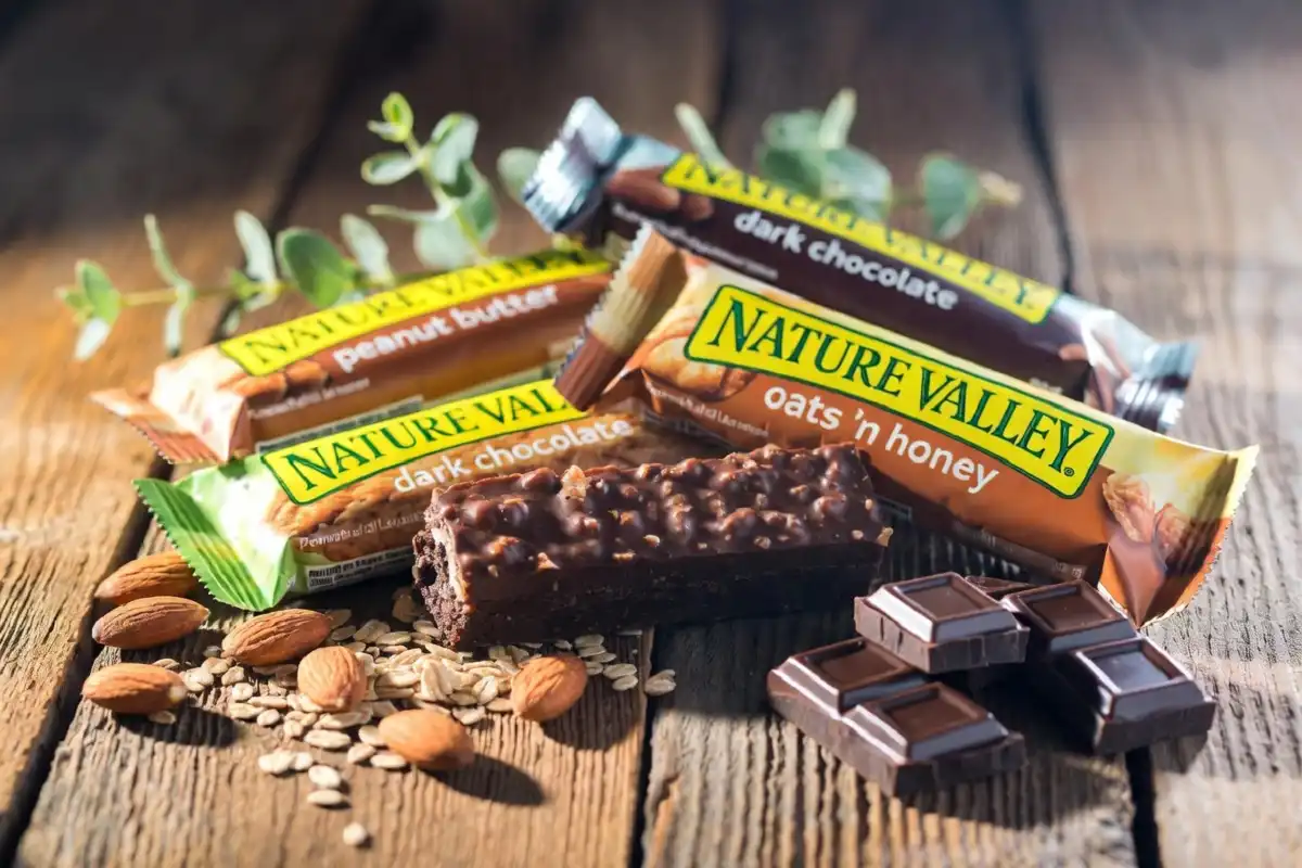 Assorted Nature Valley protein bars arranged on a wooden table with natural sunlight