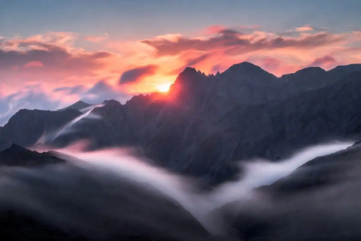 Sunrise over misty mountain peaks with orange and pink sky