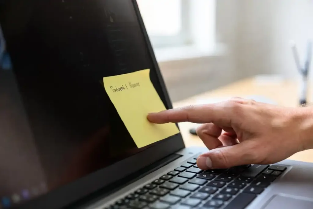 Hand placing a sticky note with a short quote on a laptop screen