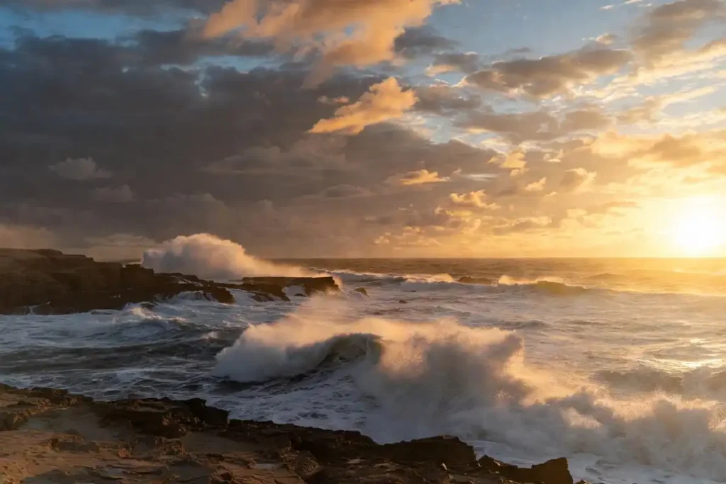 Dramatic coastline at sunset with crashing waves under bold storm clouds